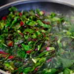 Chopped Swiss chard sautéing in a frying pan, with visible steam rising from the greens.
