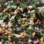 A close-up of a kale salad with feta cheese, walnuts, red onion, dried cranberries, and diced apples.