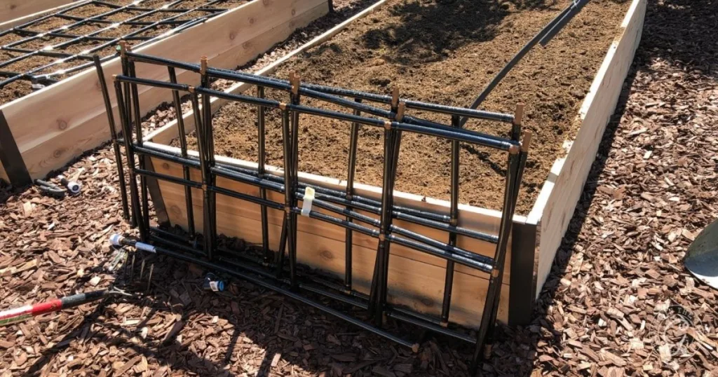 A metal trellis leans against a wooden raised garden bed, showcasing thoughtful raised bed garden design with soil and irrigation tubing neatly in place.