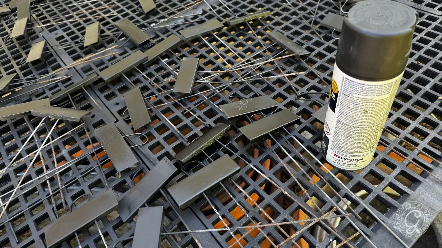 Black spray-painted metal clips drying on a plastic grid surface, with a can of black spray paint nearby.