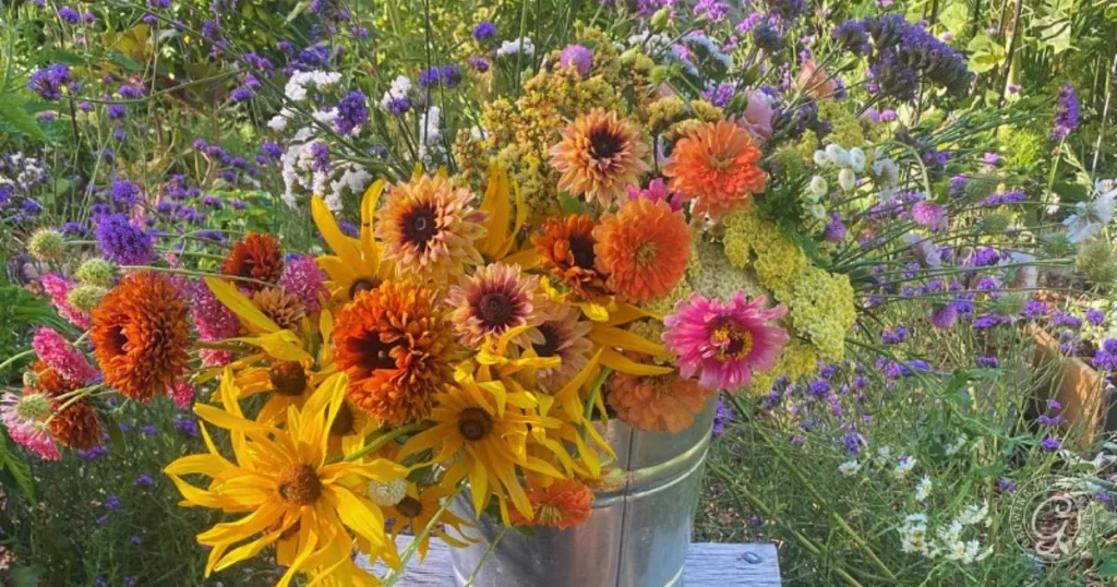 A metal bucket filled with colorful wildflowers sits outdoors among a garden of blooming flowers, showcasing quick and easy garden flower arrangements.