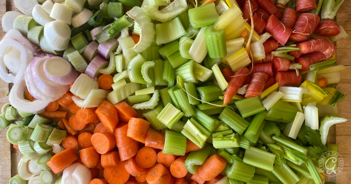 Chopped celery, carrots, onions, and colorful carrots arranged in neat sections on a wooden surface&mdash;perfect for making a fresh garden vegetable broth.