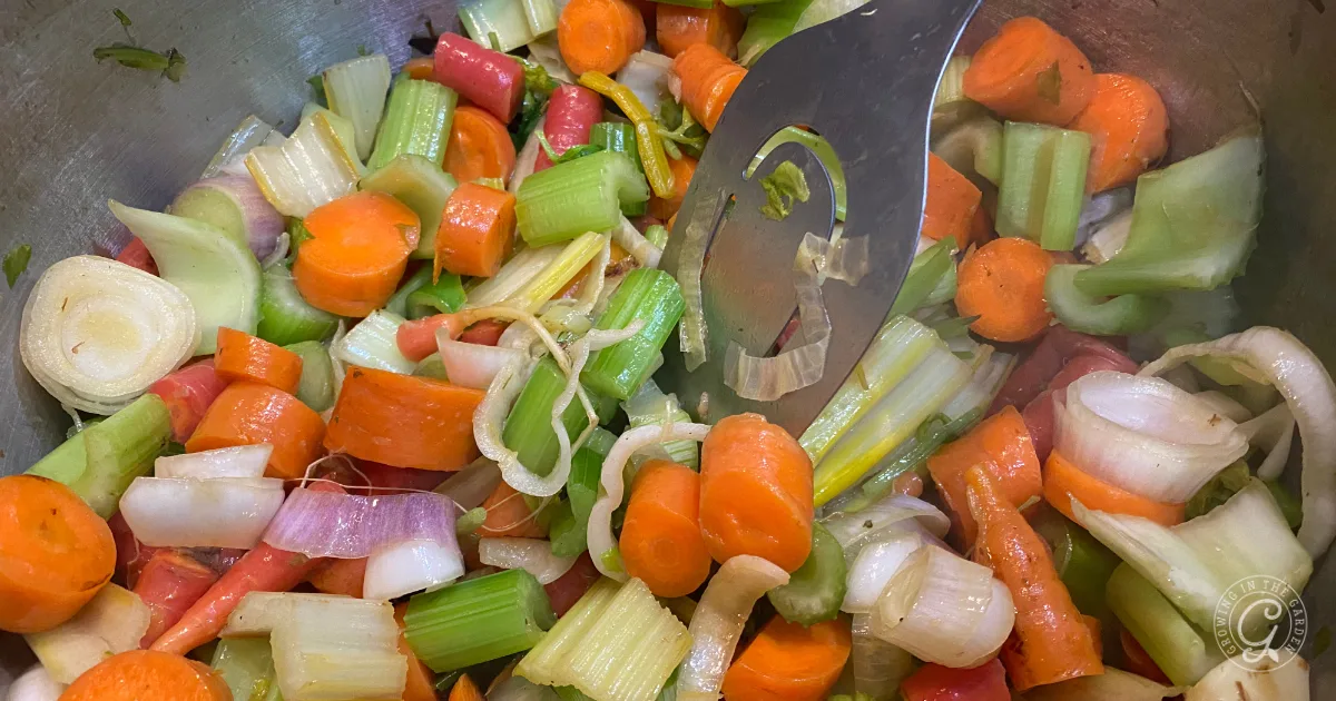 Chopped carrots, celery, and onions simmer in a pot of garden vegetable broth, stirred gently with a metal slotted spoon.