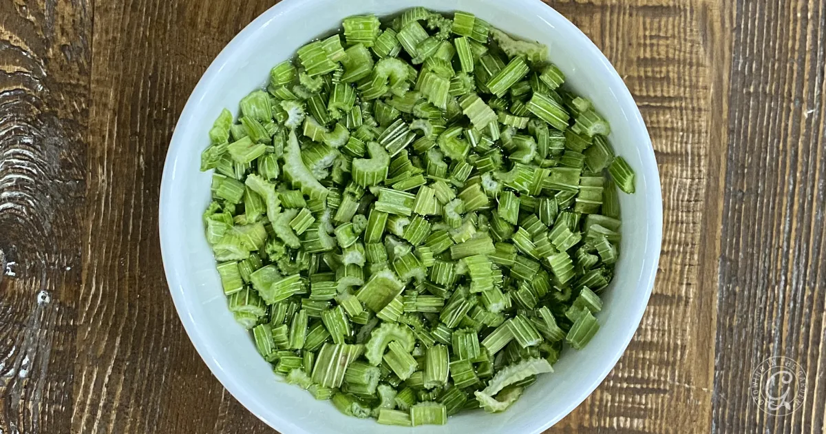 A white bowl filled with chopped green freeze dried celery sits on a wooden surface.