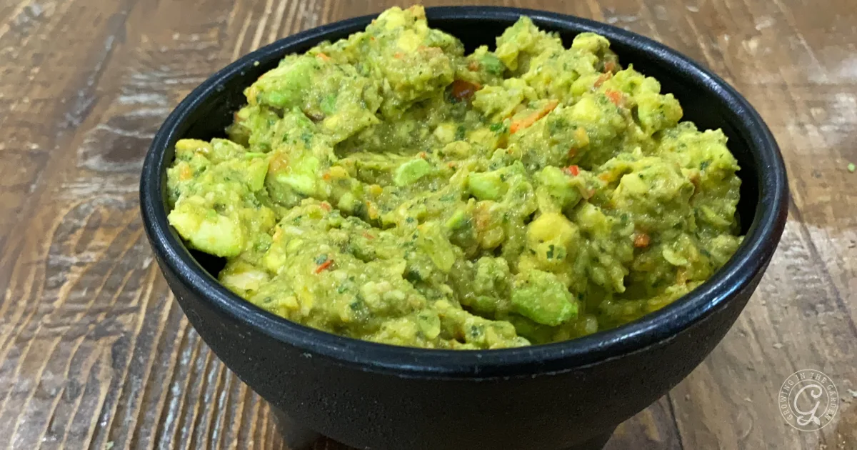 A black bowl filled with chunky guacamole and bits of freeze dried celery sits on a wooden surface.
