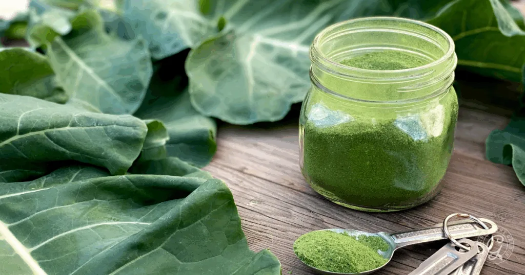 A jar of green powder with leafy greens, two measuring spoons, and wood background.
