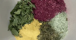 Four piles of different colored dried herbs and powders, including Roselle Citrus Tea, are arranged in a circle on a gray surface.