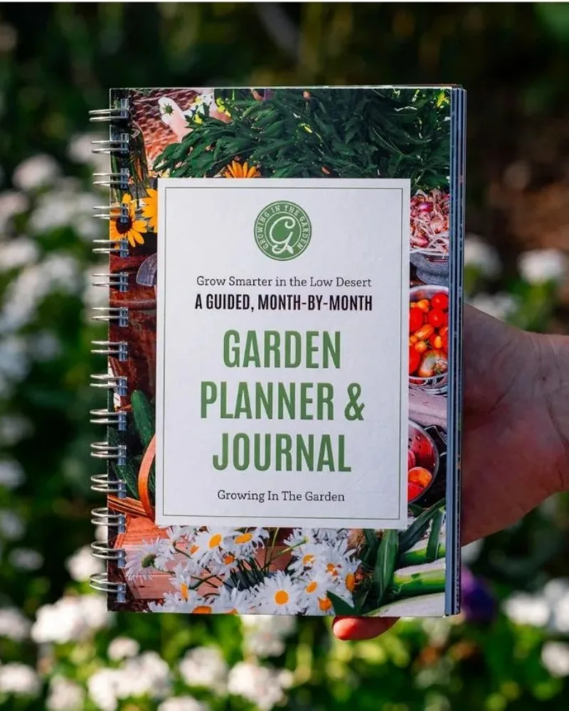 A hand holds a spiral-bound Garden Planner & Journal with a cover featuring flowers and vegetables—an ideal garden gift and one of those gift ideas that will make any gardener happy.