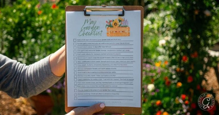 A person holds a garden checklist on a clipboard, with plants and flowers blurred in the background.