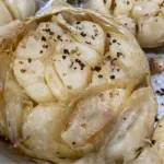 Close-up of a roasted garlic bulb with cracked black pepper sprinkled on top.