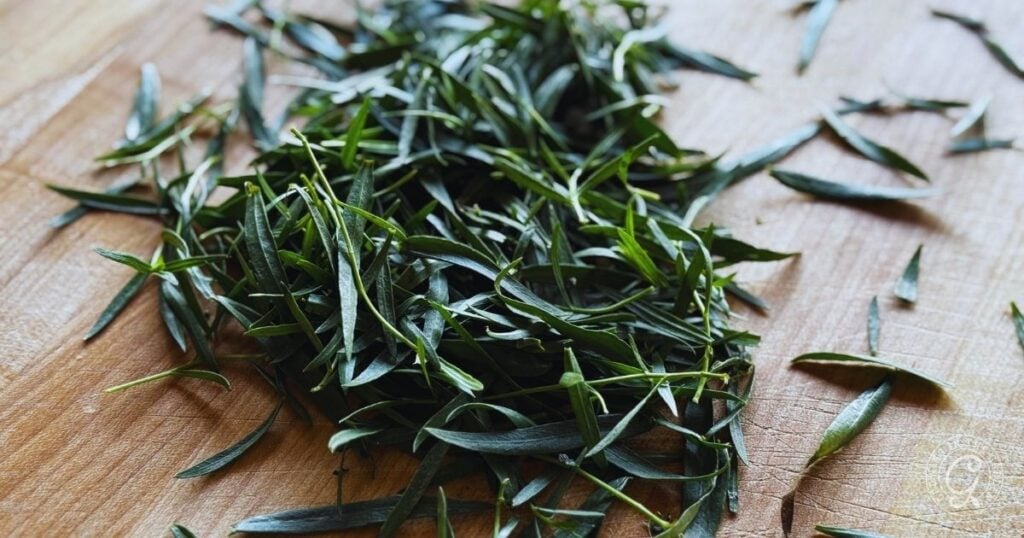 A pile of fresh French Tarragon leaves, just picked from the garden, rests on a wooden cutting board.