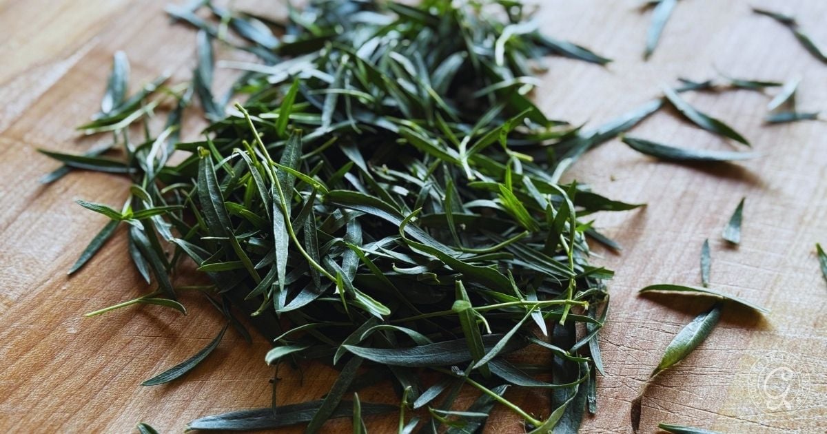 A pile of fresh French Tarragon leaves, just picked from the garden, rests on a wooden cutting board.