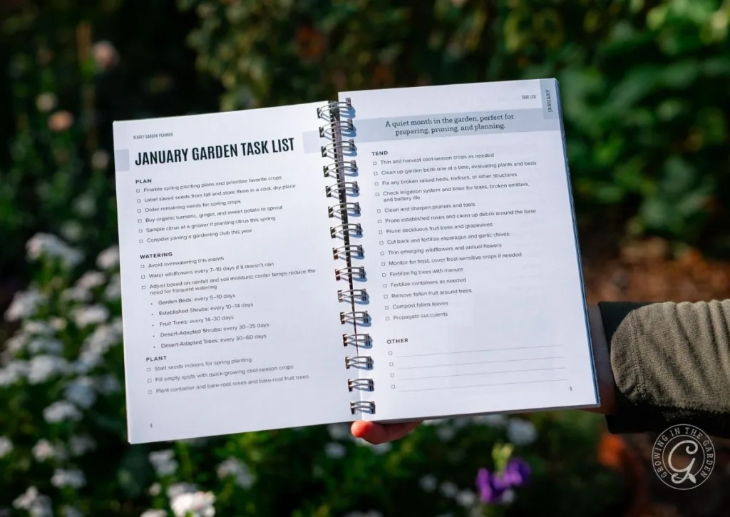 Person holding open an Arizona Garden Planner displaying a January garden task list and tips, with plants blurred in the background.