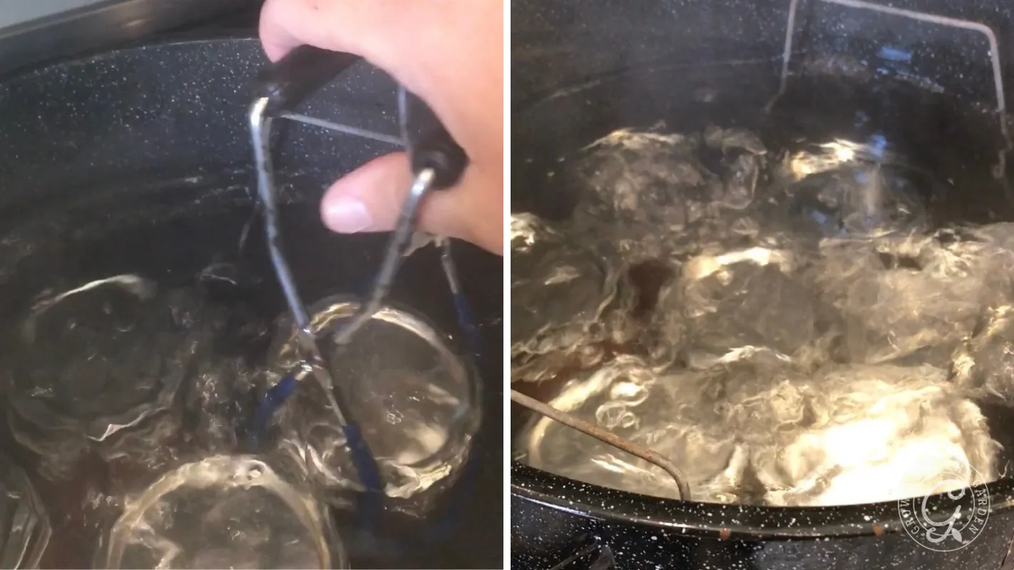 A hand uses tongs to place jars into boiling water in a large pot for canning.
