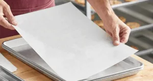 Person placing a sheet of parchment paper onto a baking tray, preparing the kitchen for delicious roasted peppers.