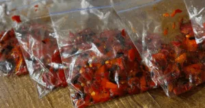Chopped roasted peppers in clear plastic bags on a wooden surface.