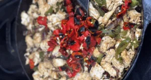 Close-up of cooked chicken with saut&eacute;ed red and green roasted peppers in a skillet.