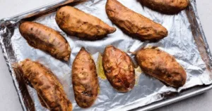 Eight baked sweet potatoes on a foil-lined baking sheet, perfect for a make ahead sweet potato casserole.
