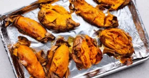 Eight baked sweet potatoes, split open on a foil-lined baking sheet—perfect for prepping a make ahead sweet potato casserole.