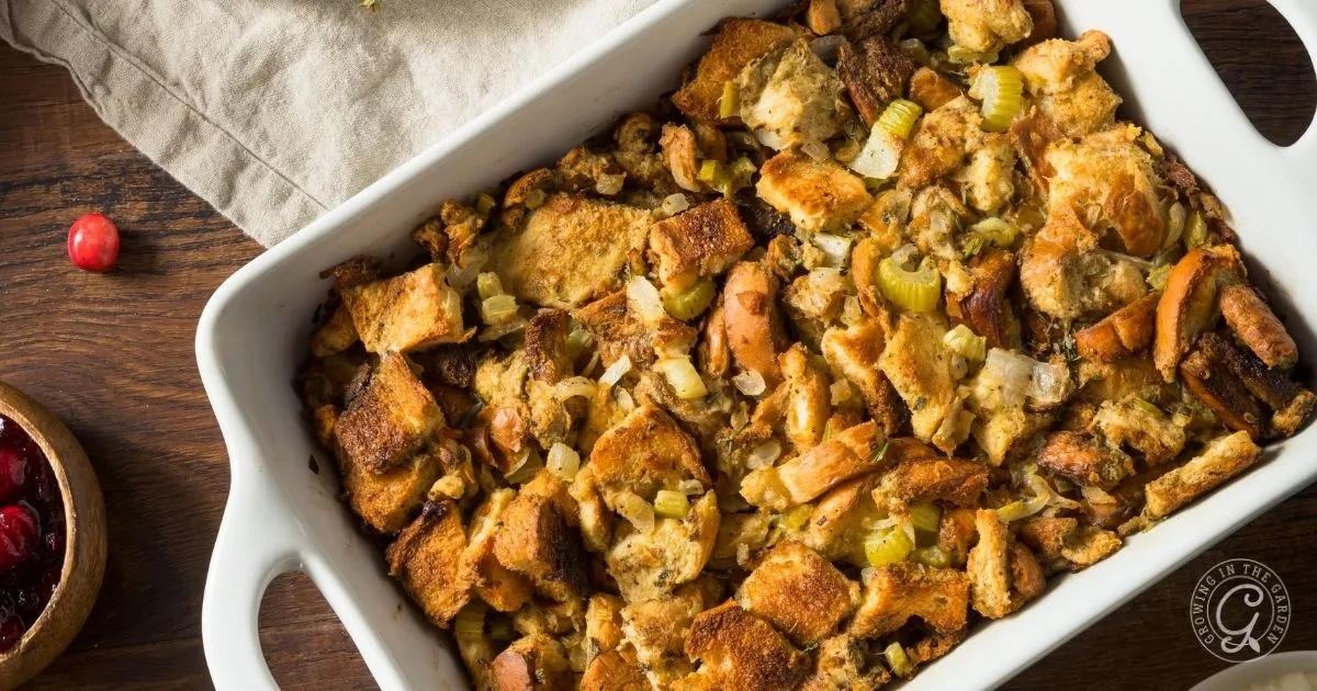 A white dish filled with Make Ahead Stuffing made of bread, celery, and onions sits on a wooden table—perfect for preparing in advance for any gathering.