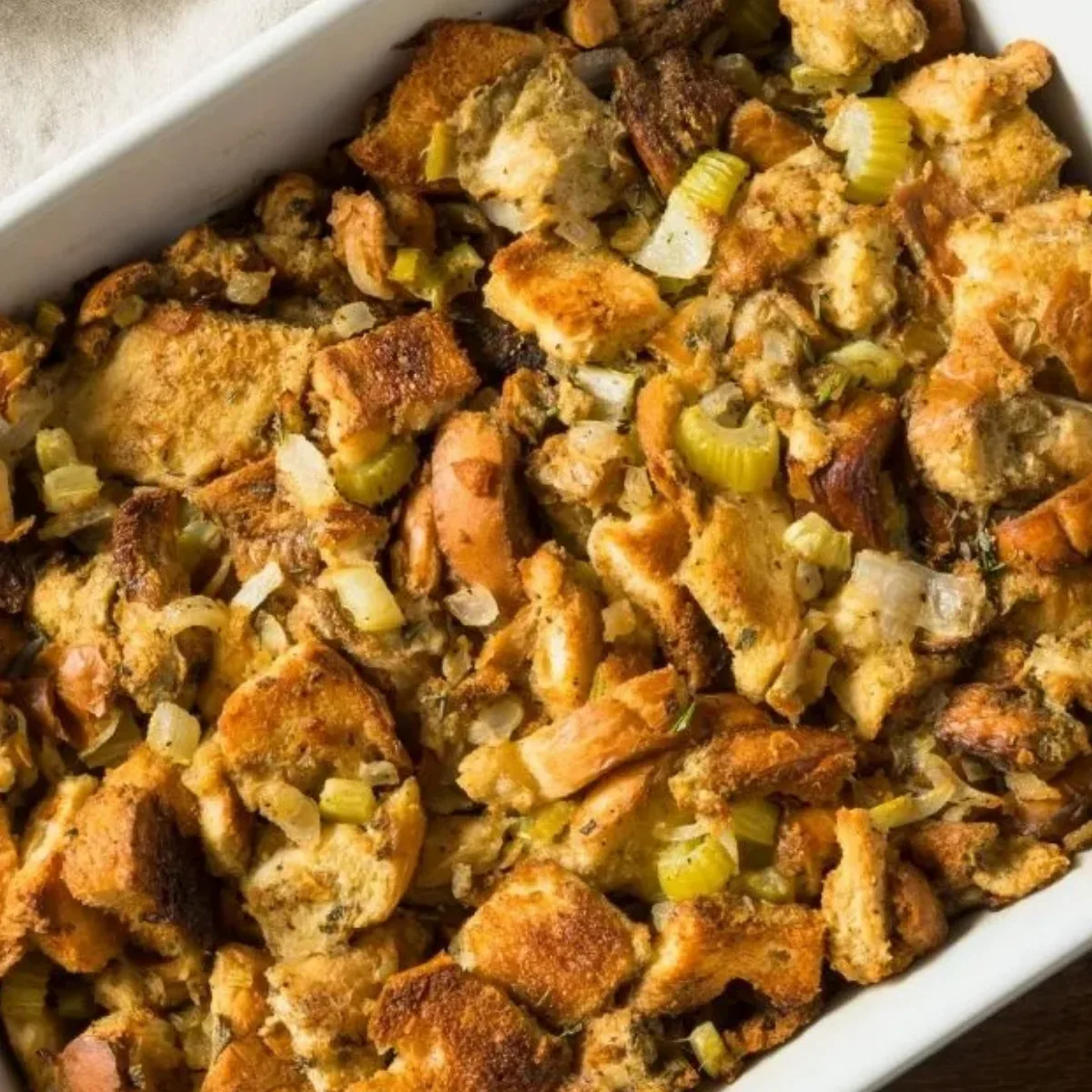 Make Ahead Sausage and Herb Stuffing Recipe features baked bread stuffing with celery and onions in a white casserole dish.