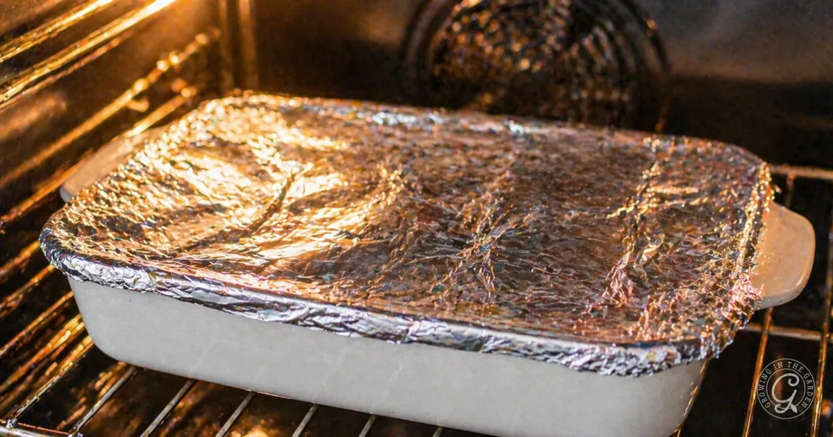 A foil-covered casserole dish, filled with Make Ahead Sausage and Herb Stuffing Recipe, is baking on a rack inside an oven.
