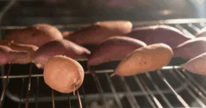 Sweet potatoes roasting on an oven rack, with sunlight shining from the back—perfect for a make ahead sweet potato casserole.