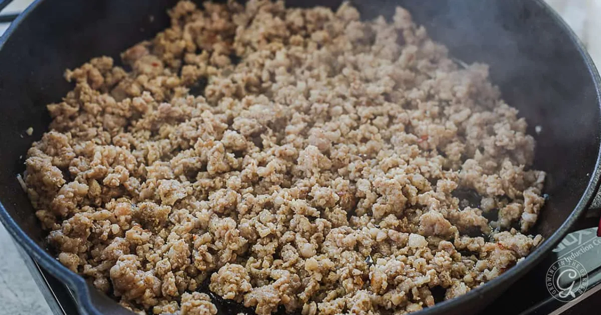 Cooked ground sausage browning in a black skillet with some steam rising. 