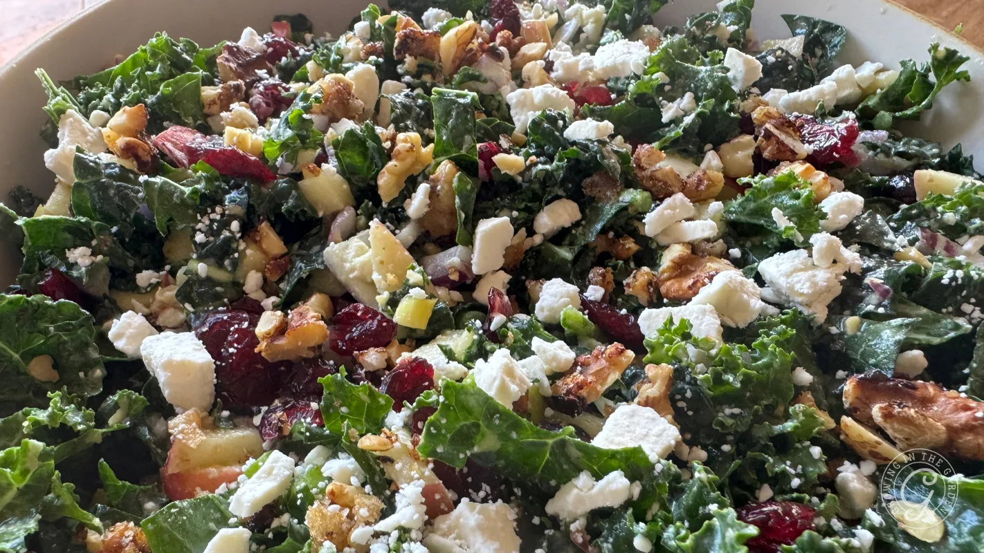 Kale salad with feta cheese, dried cranberries, walnuts, apples, and a sprinkle of dressing in a bowl.
