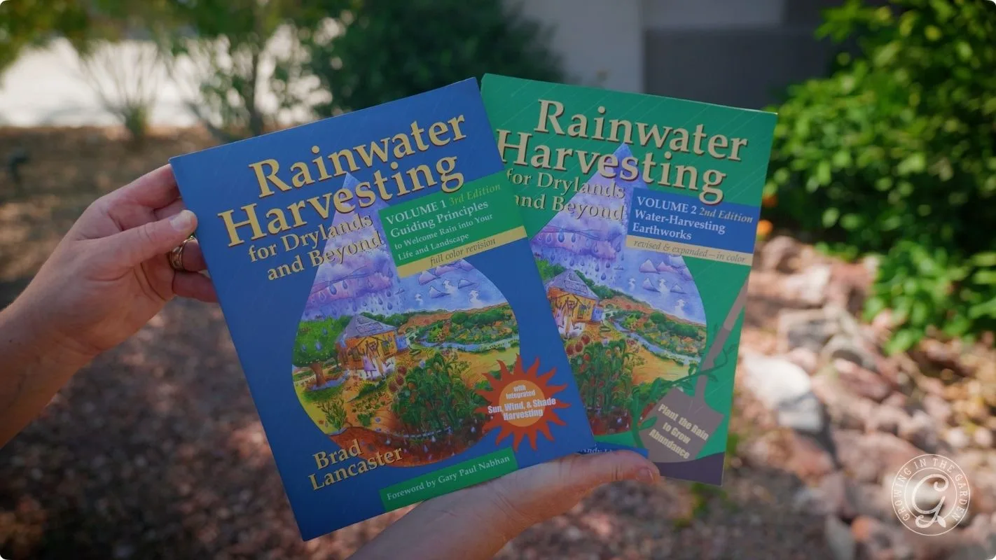 Two hands hold two Rainwater Harvesting for Drylands and Beyond books by Brad Lancaster outdoors.
