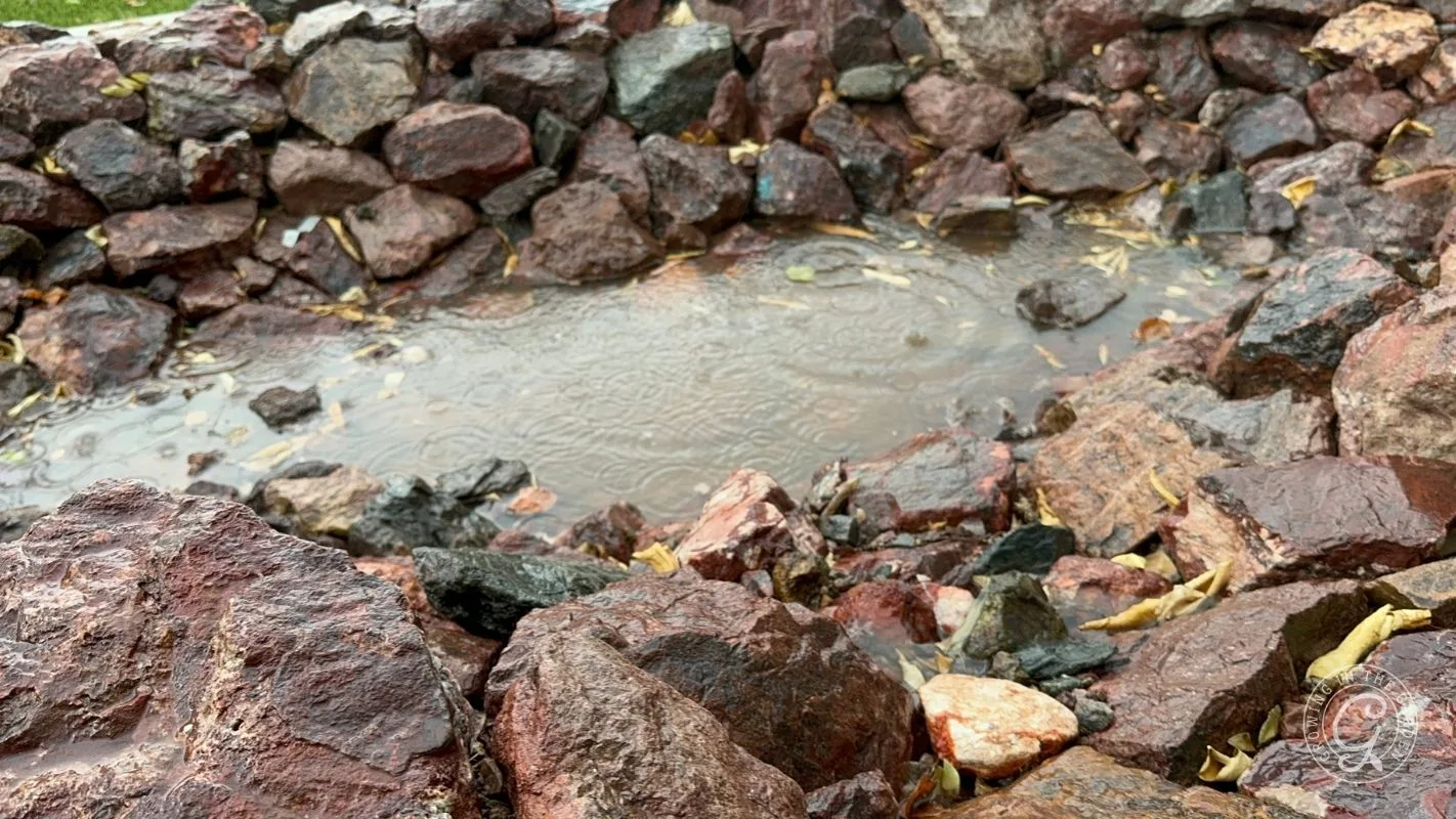 Rainwater collecting in a shallow, rocky depression surrounded by wet, reddish-brown stones.
