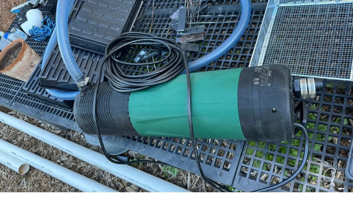 A green and black water pump with attached cables sits on a black plastic grid next to other equipment.