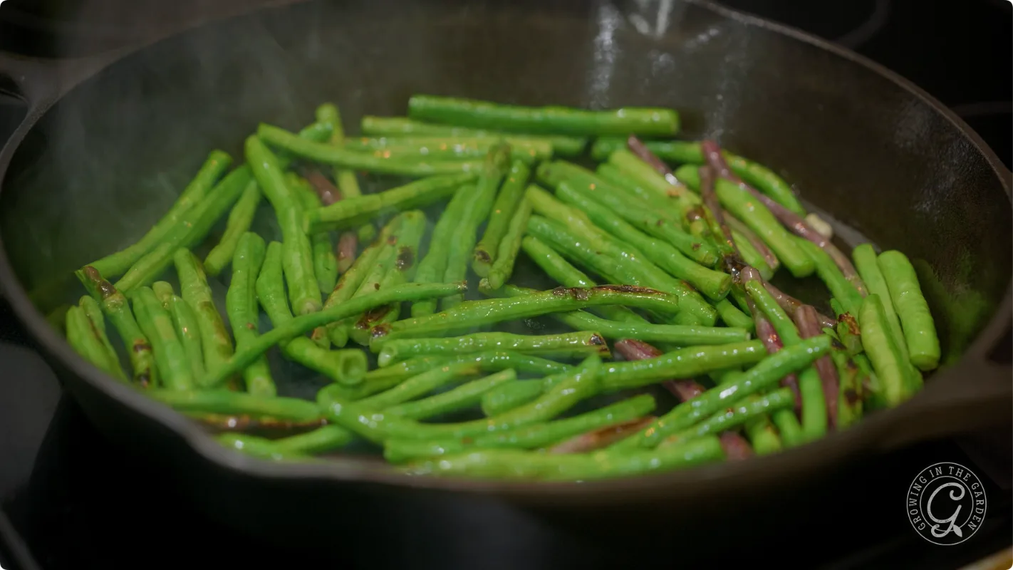 Green beans being saut&eacute;ed in a black cast iron skillet on a stovetop.