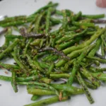 A white plate of saut&eacute;ed green beans with seasonings and spices, held up close to the camera.