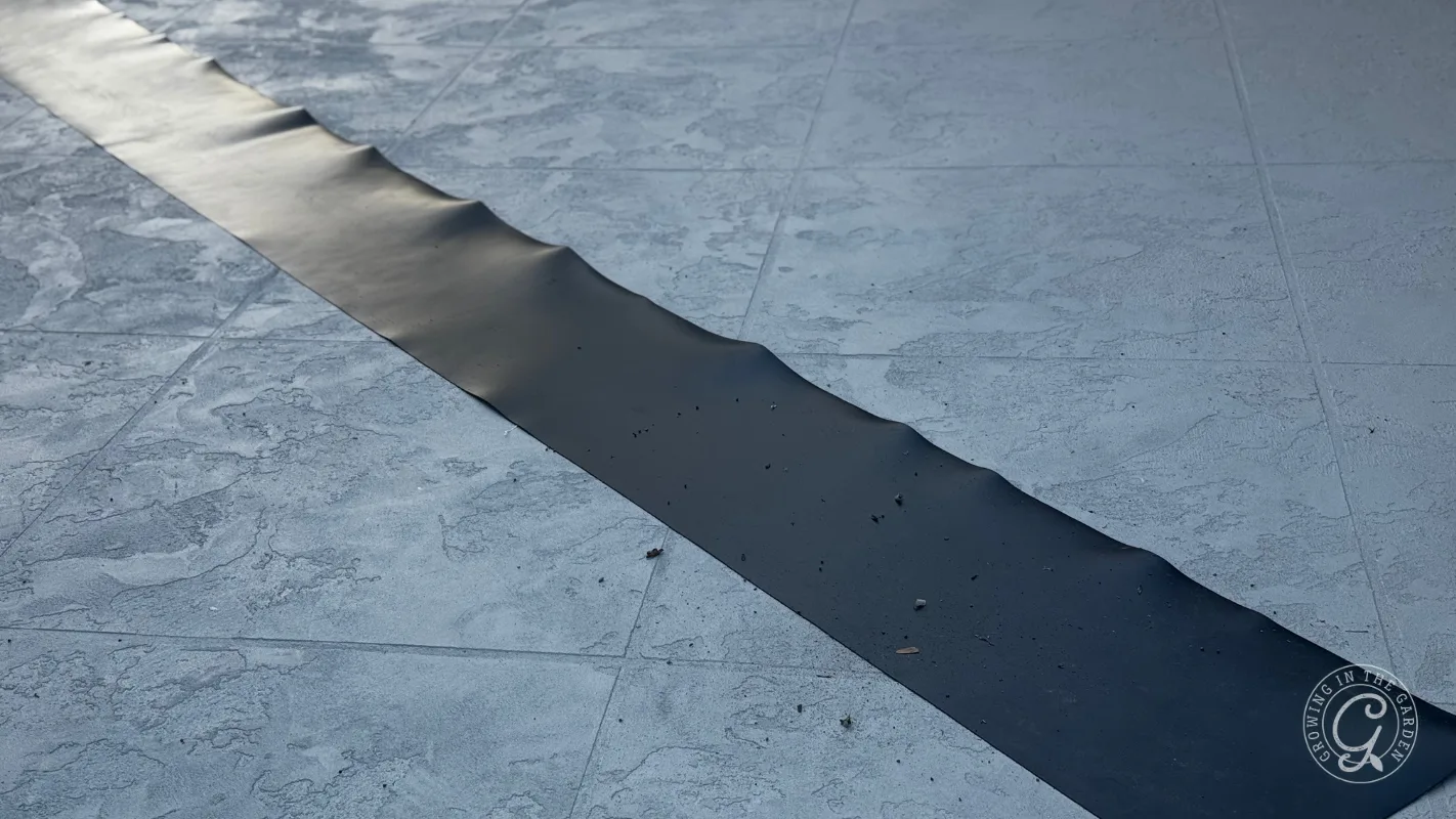 A black metal strip with slight waves runs diagonally across a textured gray tiled surface.