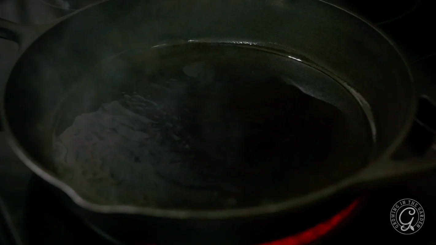 A cast iron skillet with oil heating and shimmering on a stovetop burner.