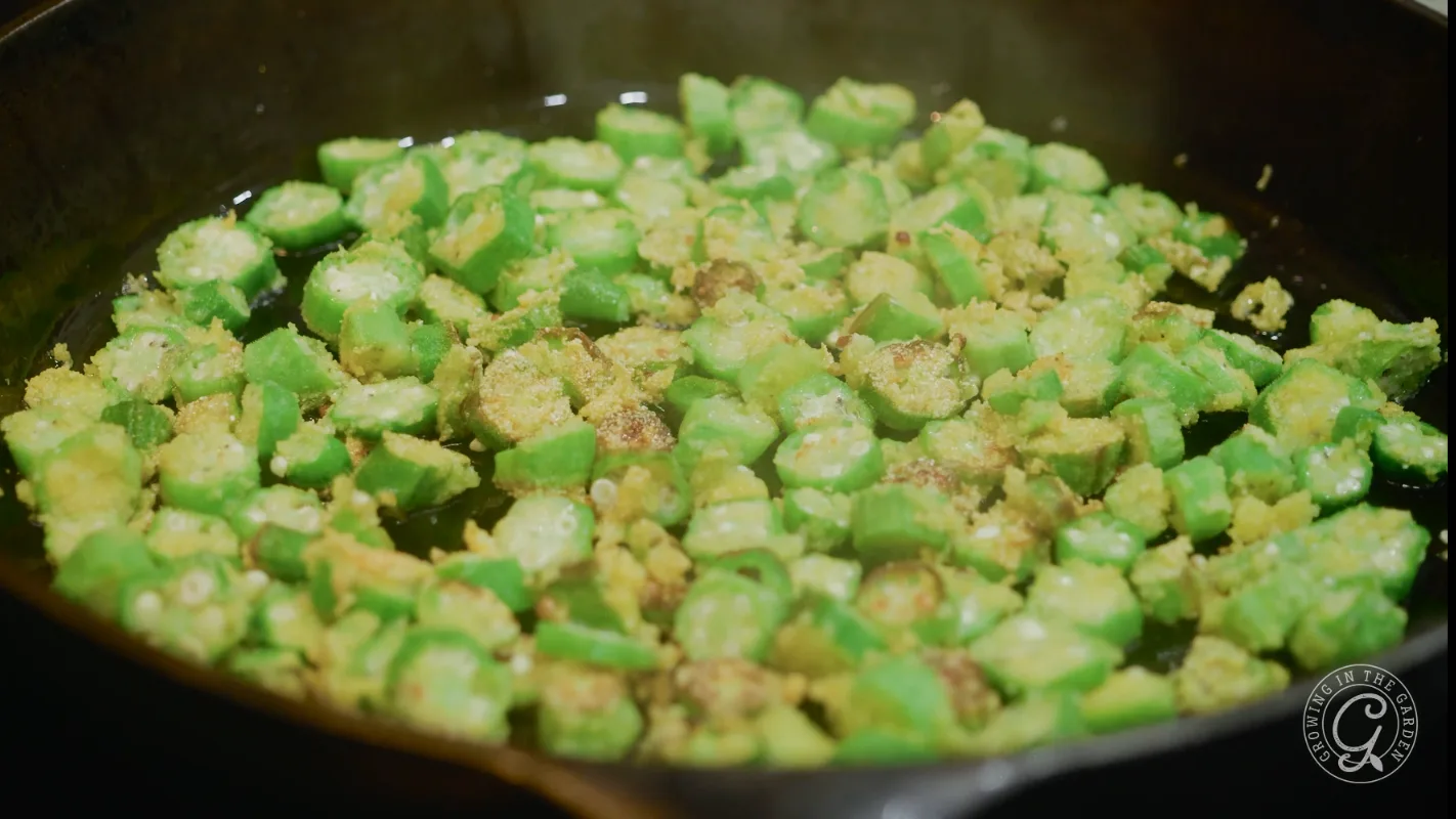 Sliced okra pieces frying in oil in a black skillet.