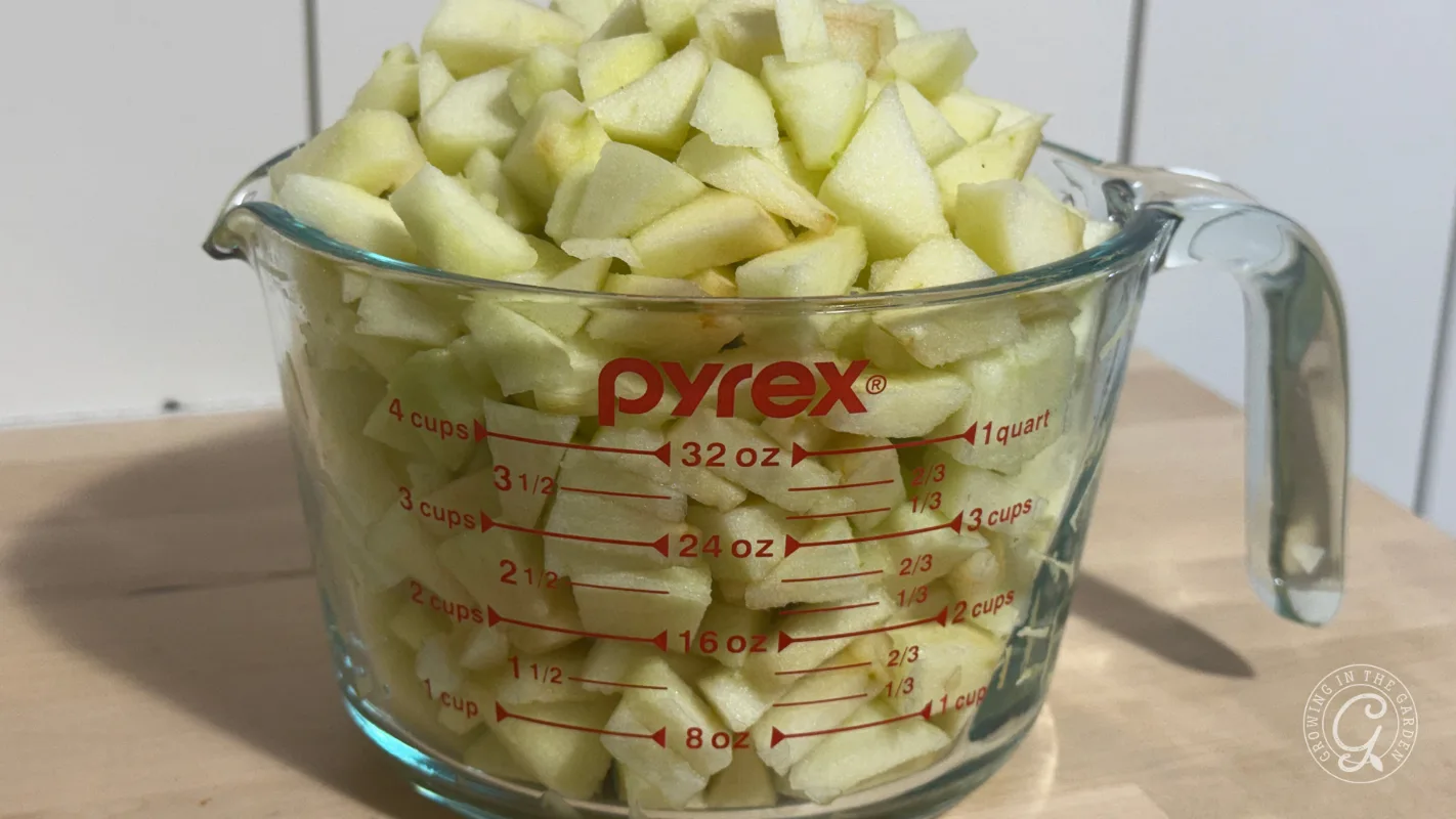 Chopped green apples fill a glass Pyrex measuring cup up to the 4-cup mark on a wooden surface.