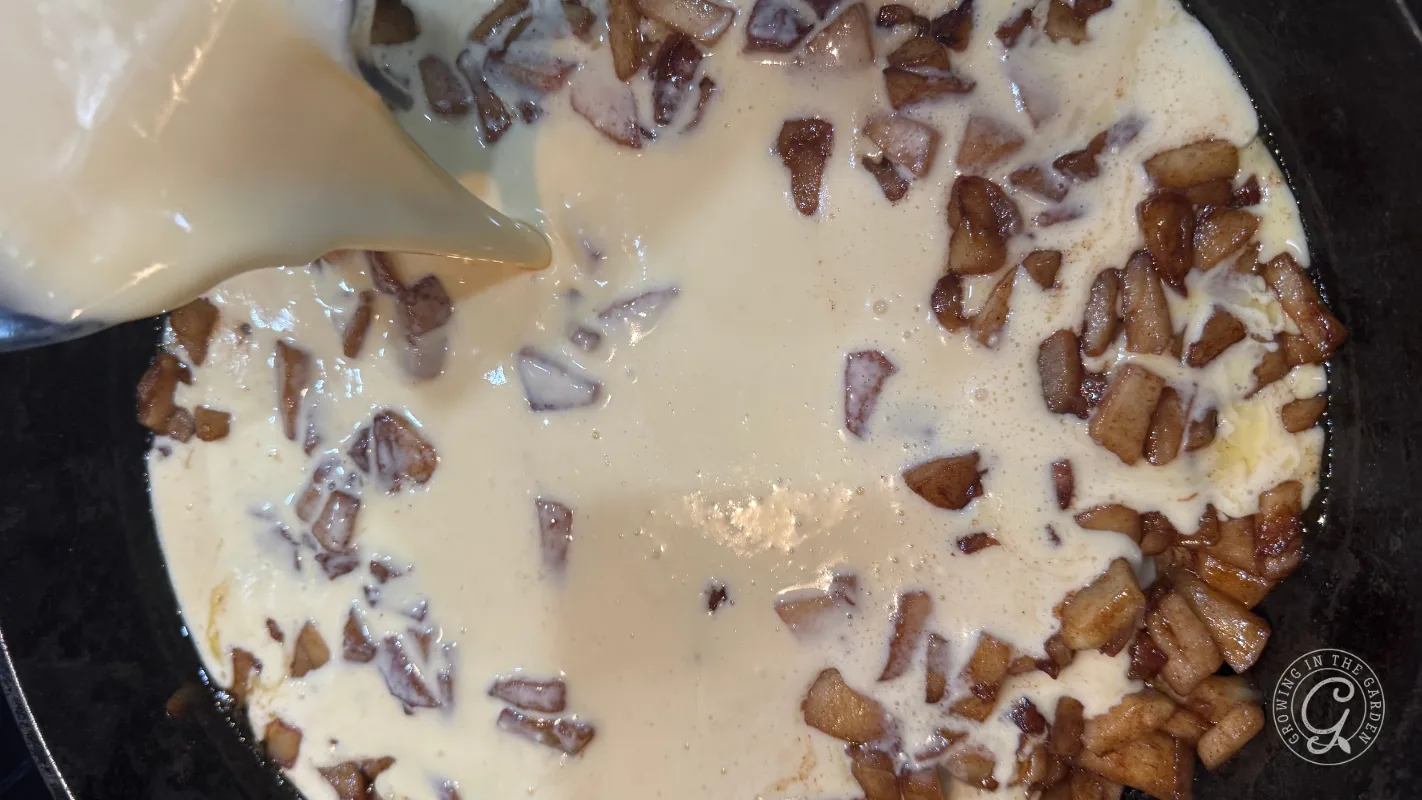 Cream is being poured over diced, cooked apples in a pan, creating a creamy mixture.
